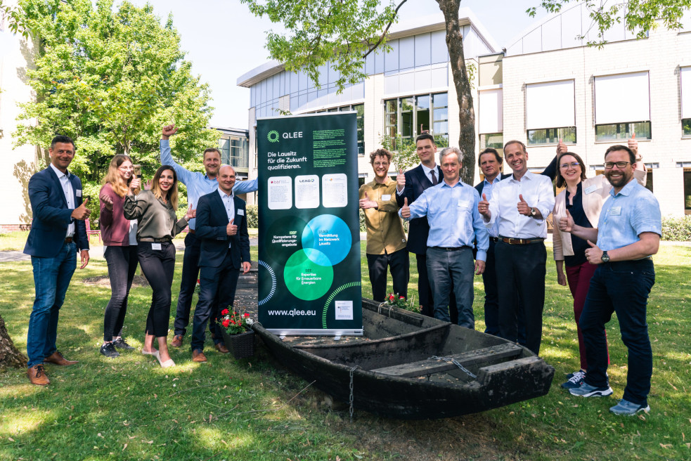 Eine Gruppe von Personen steht im Freien und posiert neben einem ausziehbaren Aufsteller mit der Aufschrift "QLEE - Die Lausitz für die Zukunft Qualifizieren".