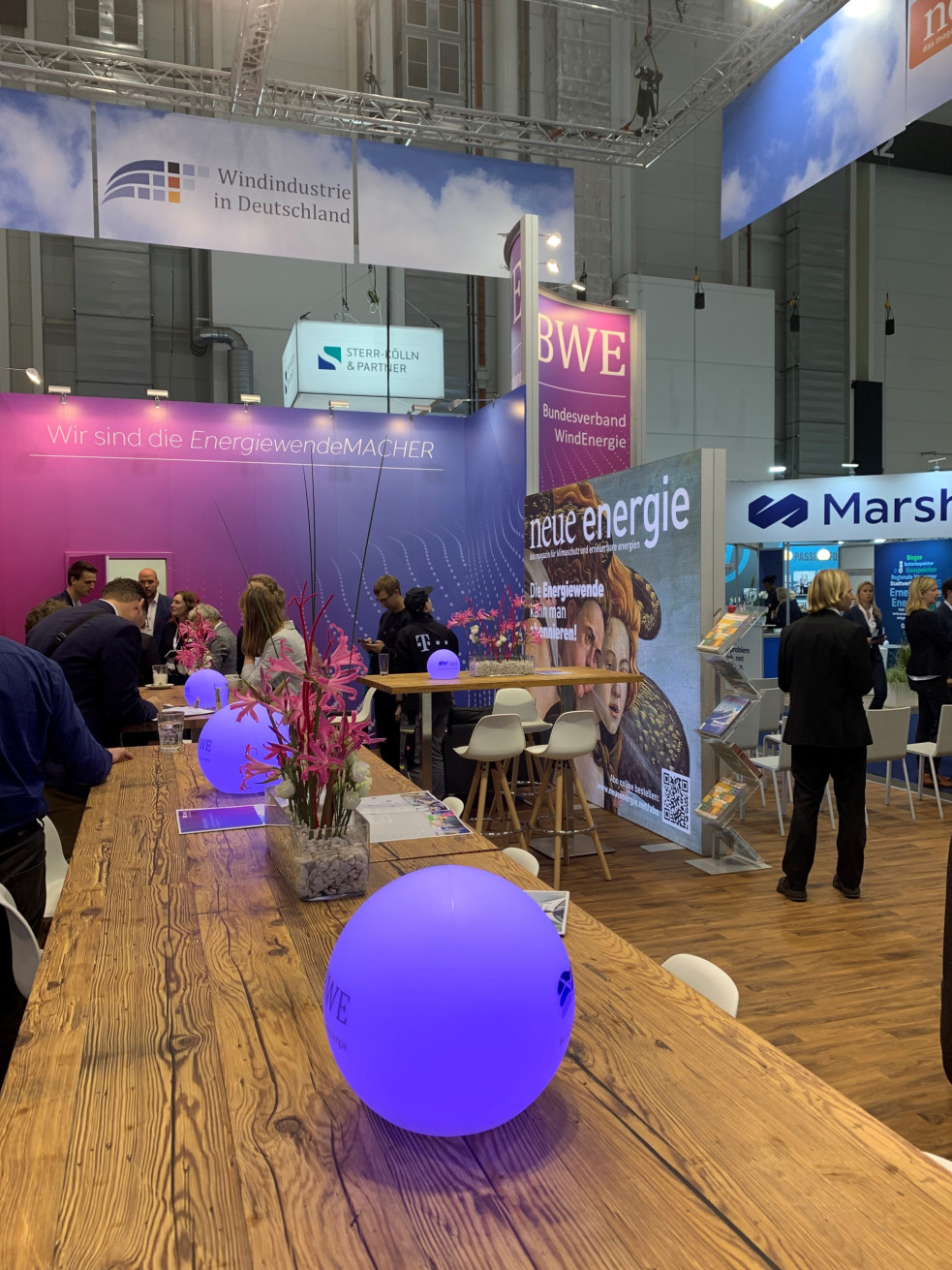 Aktuelles_WindEnergyHamburg_Credits_Vaulina_ Foto von der Messe 'WindEnergy Hamburg' mit verschiedenen Ausstellerständen und Besuchern, die sich auf der Messe umsehen.
