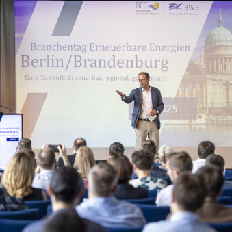 BTBB25_Bühne Großer Konferenzsaal mit Bühne im Hintergrund, auf der eine Person steht. Im Vordergrund ist das Publikum zu sehen.