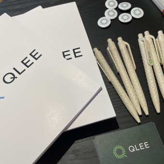 QLEE-Merch Foto von QLEE-Merchandise, weiße Blöcke und Stifte mit QLEE-Logo.