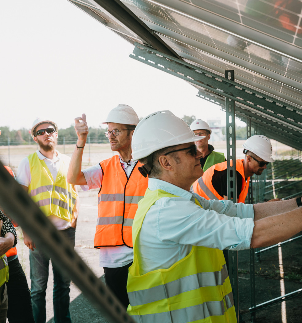 Personen mit Warnweste und Sicherheitshelm inspizieren eine Solaranlage